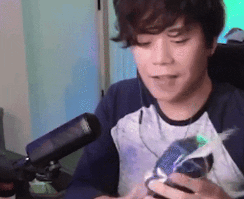 a young man is sitting in front of a microphone holding a cell phone .