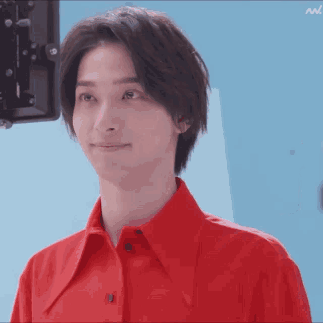a man wearing a red shirt is smiling in front of a blue background
