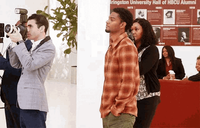 a man taking a picture of a man in front of a burlington university hall of hbcu alumni poster