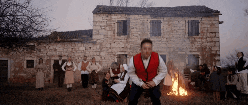 a man in a red vest squats in front of a group of people