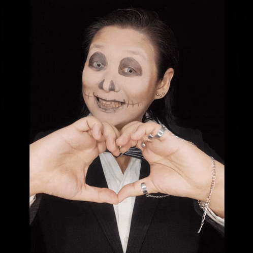a woman with a skeleton makeup on her face making a heart with her hands
