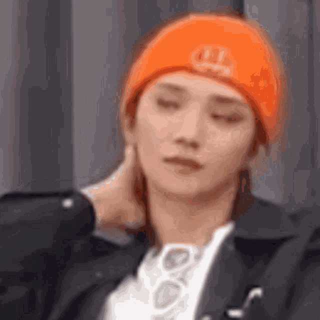 a man wearing an orange beanie and a black jacket is holding his neck .