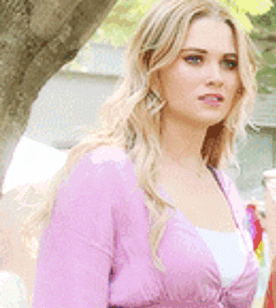 a blonde woman in a pink sweater is standing in front of a tree