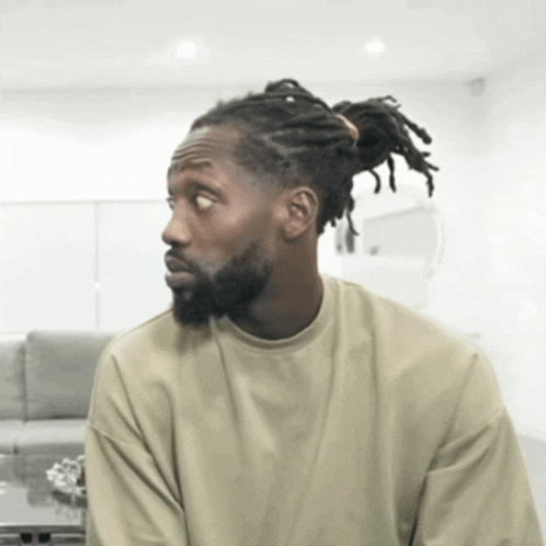 a man with dreadlocks and a beard is wearing a tan sweatshirt