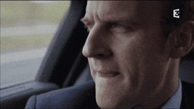 a man in a suit is sitting in the back seat of a car with the letters e3 on the bottom right
