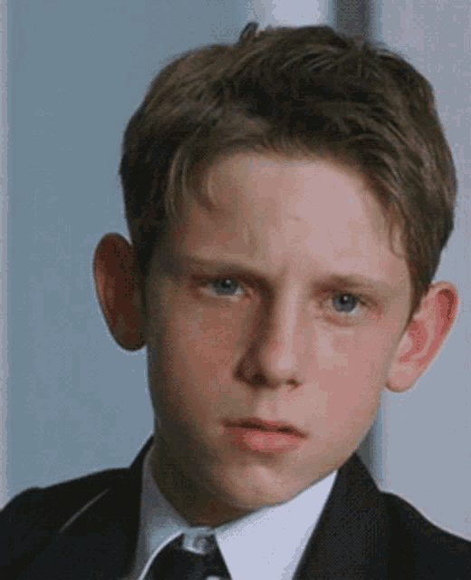 a young boy in a suit and tie looks at the camera .