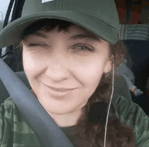 a woman wearing a green hat and ear buds winks at the camera