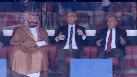 three men are sitting in a stadium and one is wearing a turban