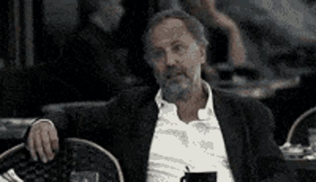 a man with a beard is sitting in a chair with his arm resting on a table .