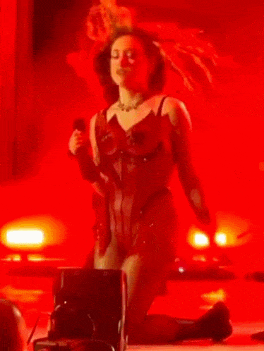 a woman in a red dress is kneeling down on the floor on a stage .