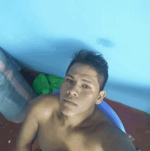 a shirtless man sits in a blue chair with a blue wall behind him