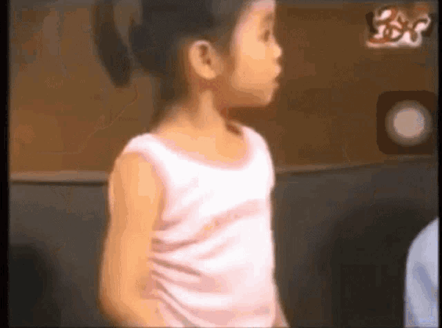 a little girl in a pink tank top is standing in front of a wall with the word love on it .