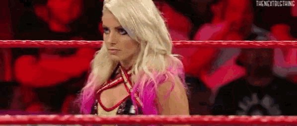a woman with pink hair is standing in a wrestling ring looking at the camera .