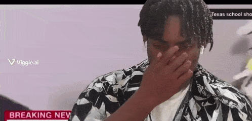 a man is covering his face with his hand in front of a breaking news sign .