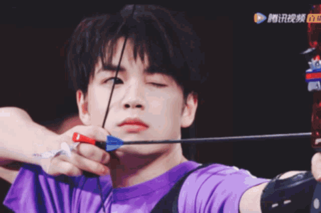a man in a purple shirt is holding a bow and arrow in his right hand