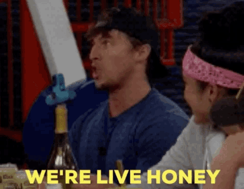 a man and a woman are sitting at a table with a bottle of wine and the words we 're live honey .