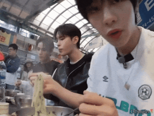 a man wearing a umbro shirt is eating noodles with chopsticks