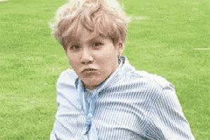 a young man in a striped shirt is making a funny face while sitting in the grass .