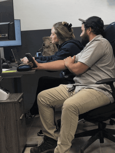 a man and a woman sit at a desk looking at a phone