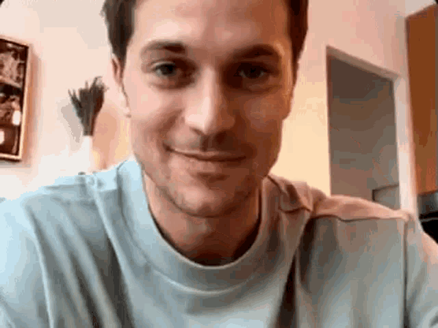 a man in a blue t-shirt is smiling and looking at the camera .