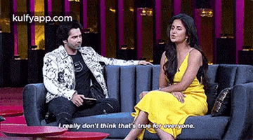 a man and a woman are sitting on a couch talking . the woman is wearing a yellow dress .
