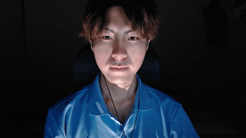 a man in a blue shirt is making a funny face in the dark