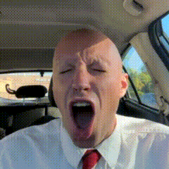 a bald man in a white shirt and red tie is yawning while sitting in a car