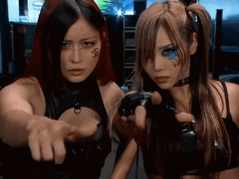 two women are standing next to each other and one is pointing at the camera .