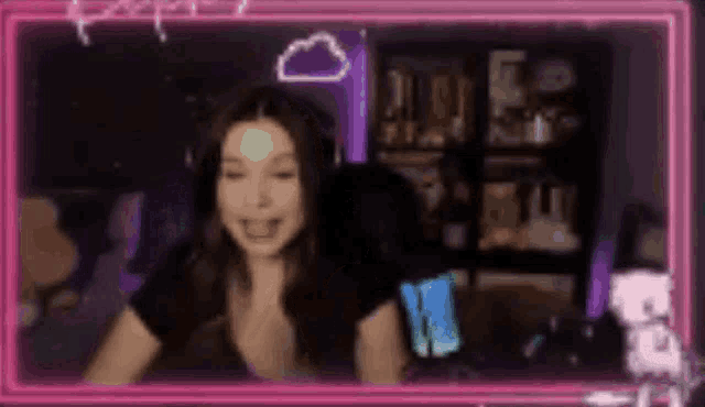 a woman is sitting in front of a computer screen with a pink neon frame around her .