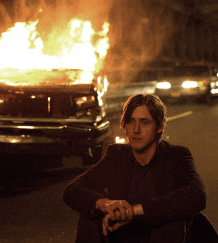 a man sits in front of a burning vehicle