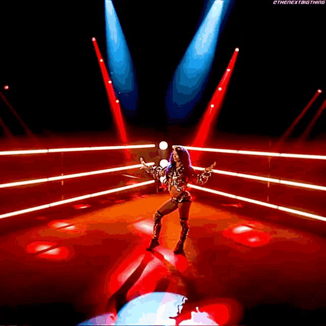 a woman in a wrestling outfit is standing in the middle of a ring surrounded by red lights