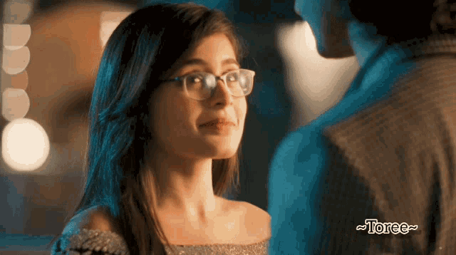a woman wearing glasses is looking at a man in a suit with the word torce below her