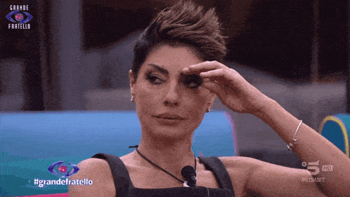 a woman wipes her eye with her hand while watching a television show called grande fratello