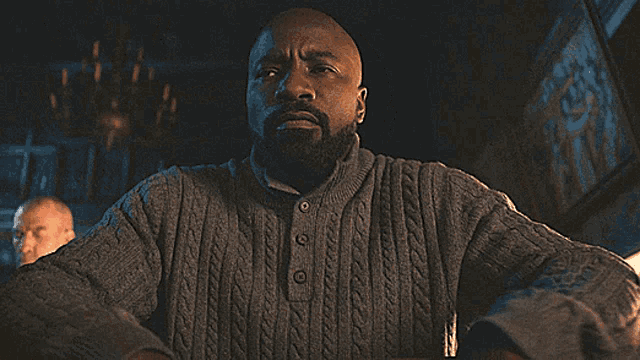 a man in a grey sweater is sitting at a table and says fuckity fuck fuck fuck