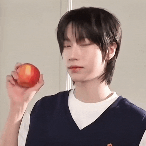 a young man is holding an apple in his hand and making a funny face .