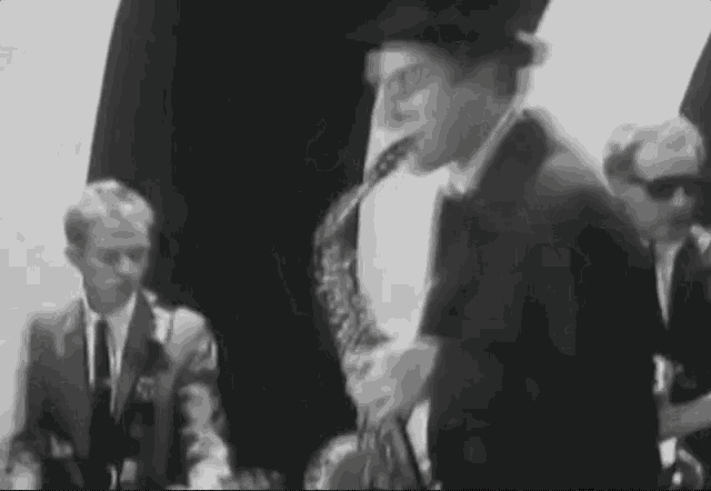 a man in a hat is playing a saxophone in a black and white photo .
