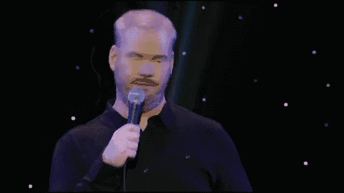 a man with a beard is holding a microphone and giving a speech on stage .