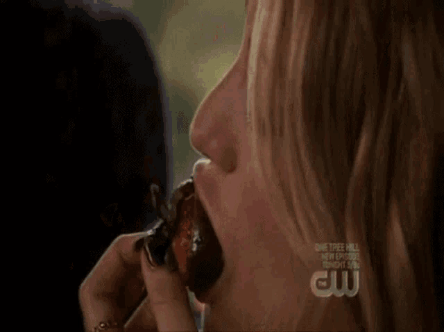 a close up of a woman eating a strawberry with a cw logo behind her