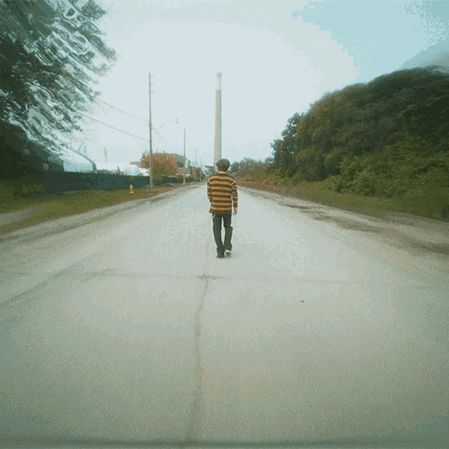 a man in a striped sweater walks down a road