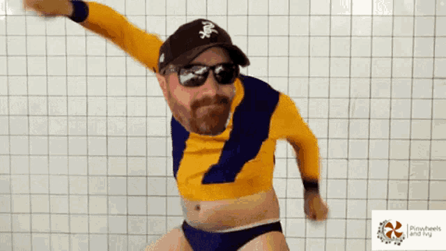 a man wearing sunglasses and a hat is dancing in front of a white tiled wall