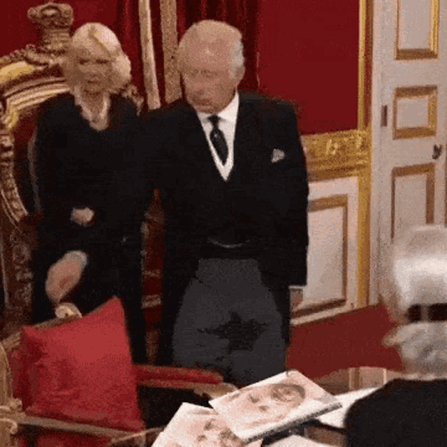 a man in a suit is standing next to a woman in a chair