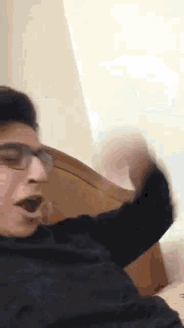 a man wearing glasses is making a funny face while sitting on a couch