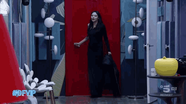 a woman in a black dress stands in front of a red door that says 5 hd