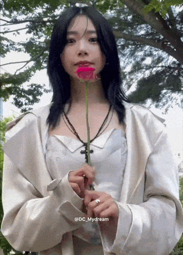 a woman in a white jacket is holding a red rose in front of her mouth .