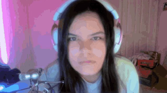 a woman wearing headphones looks at the camera in a pink room