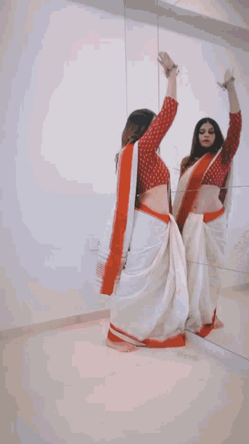 a woman in a white and red saree is dancing in front of a mirror ..
