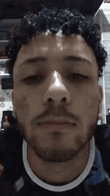 a man with curly hair and a beard is looking at the camera with his eyes closed .