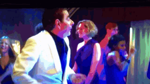 a man in a white suit is dancing with a woman in a blue dress at a party