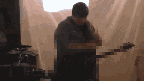a man is playing a guitar in front of a white curtain