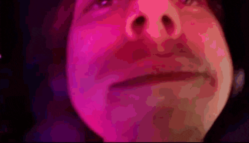 a close up of a person 's face with pink and purple lights behind them